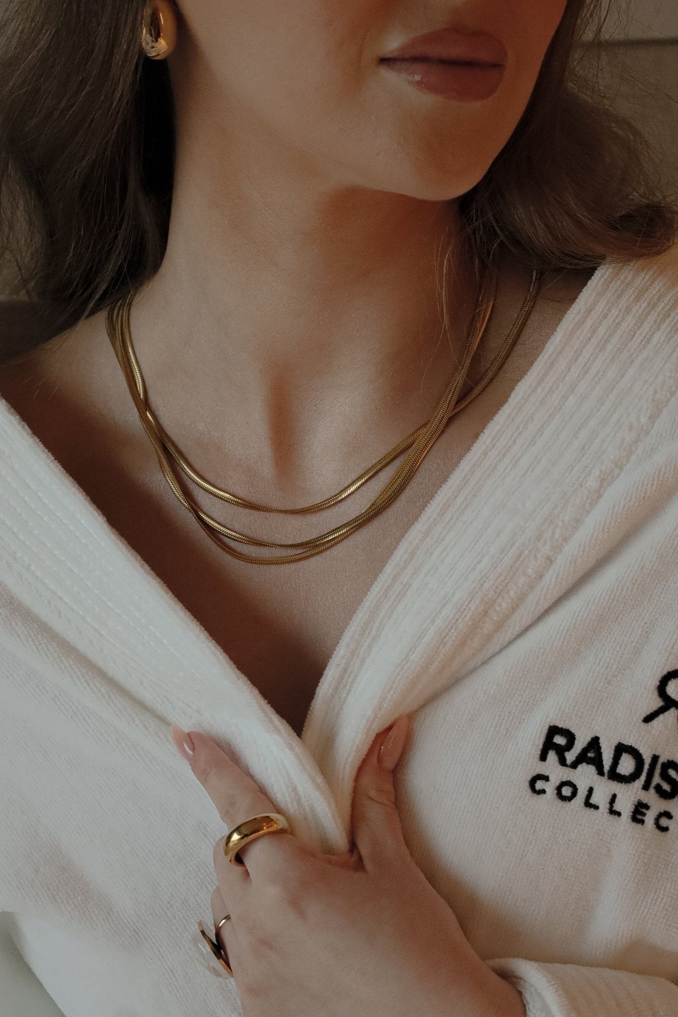 Collier doré porté par une femme vêtue d’un peignoir.