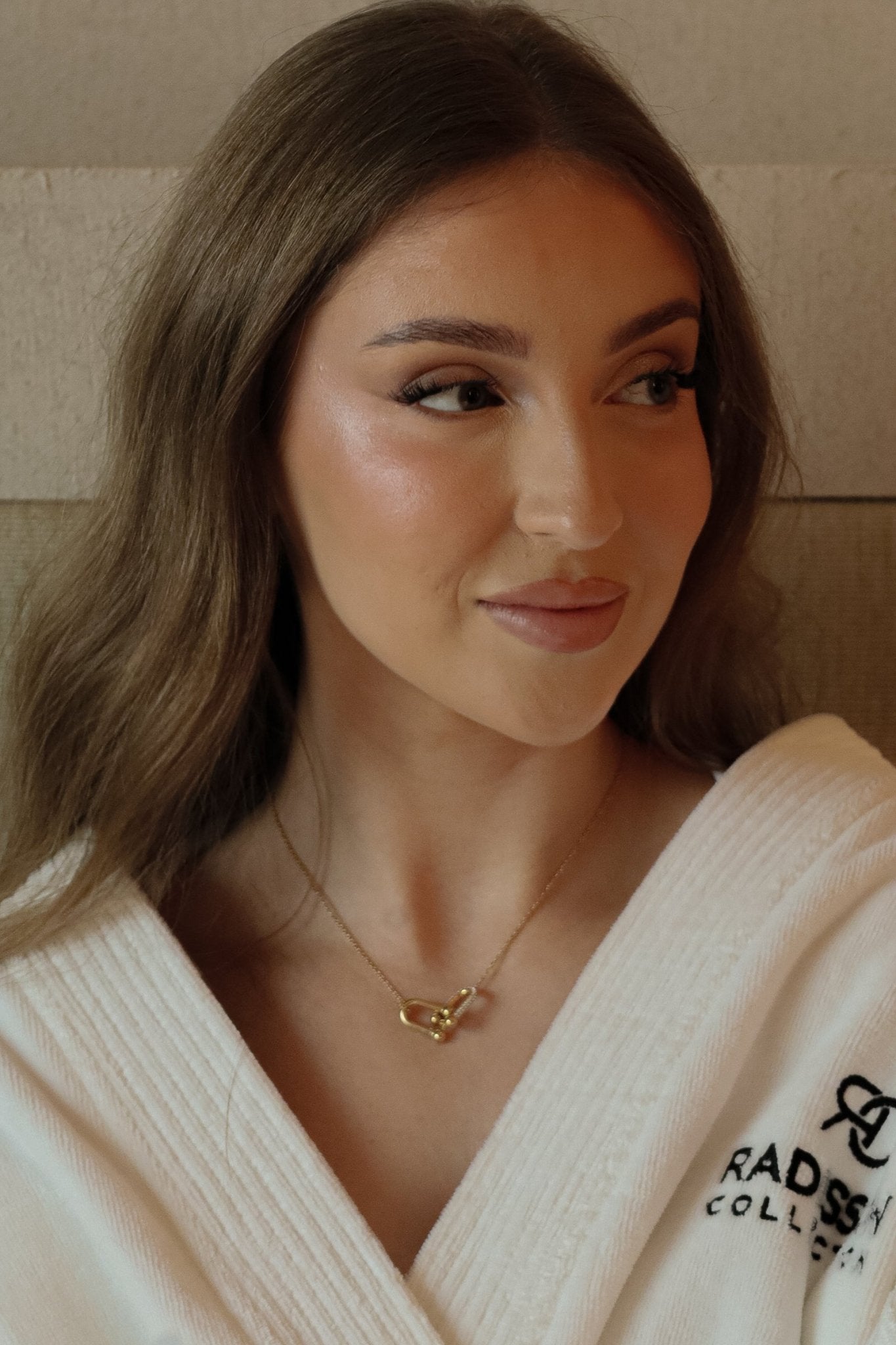 Femme souriante en peignoir blanc portant un collier doré en acier inoxydable