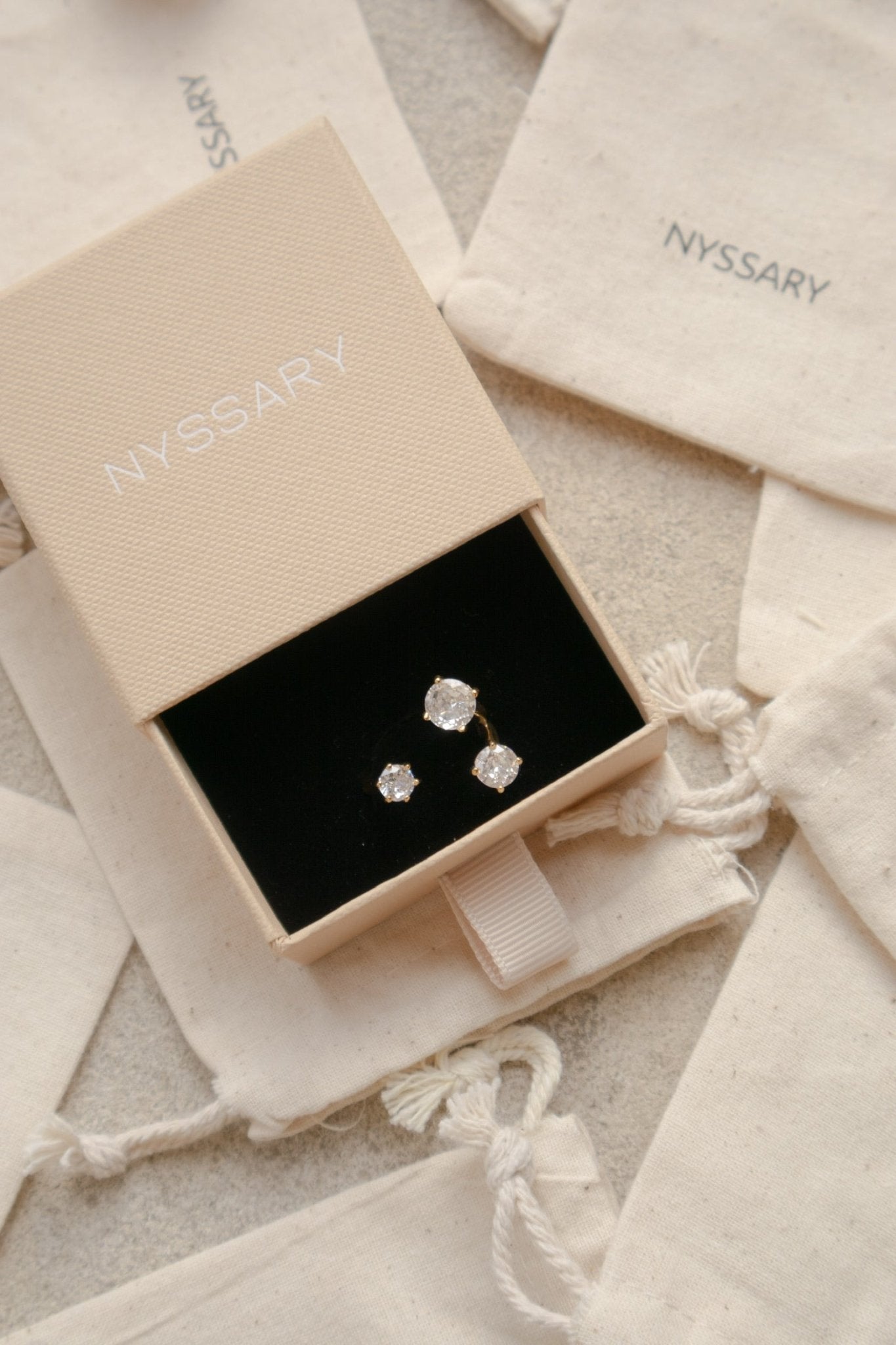Bague acier inoxydable Rhode à cristaux lumineux posée sur des pochettes Nyssary