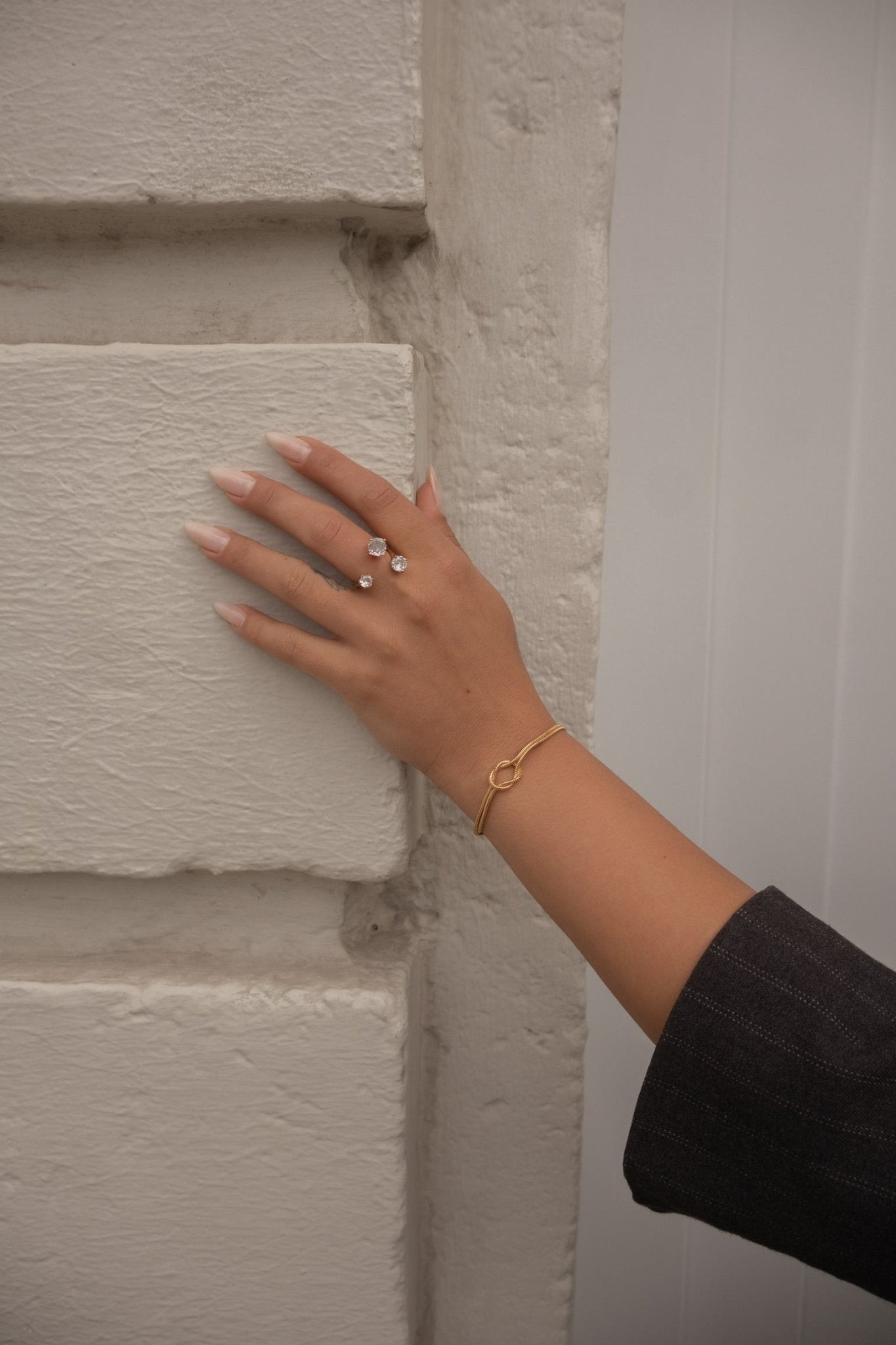 Bague en acier inoxydable dorée portée au doigt, main posée contre un mur blanc