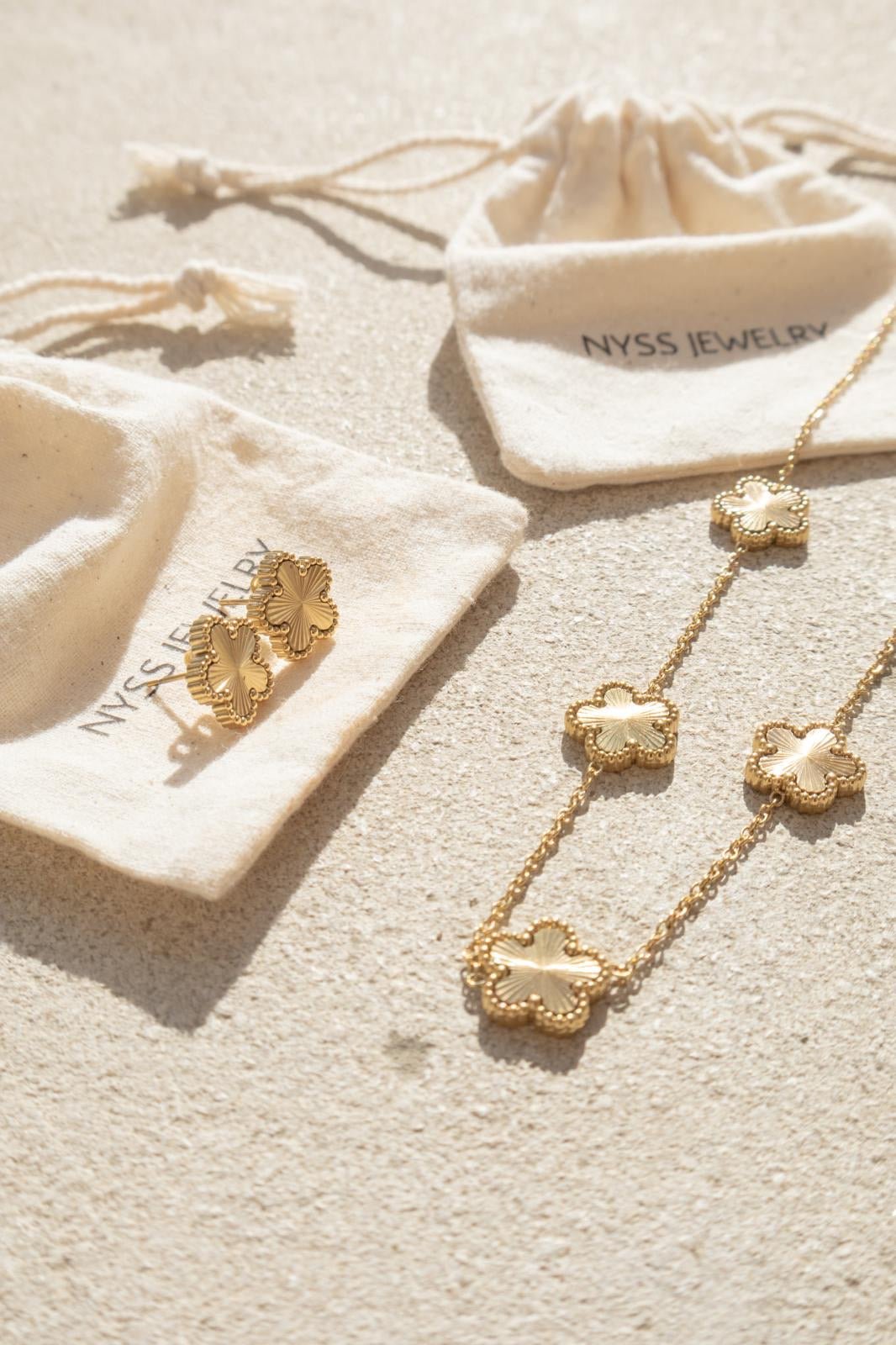 Boucles d’oreilles dorées Jasmine présentées sur des pochettes Nyssary