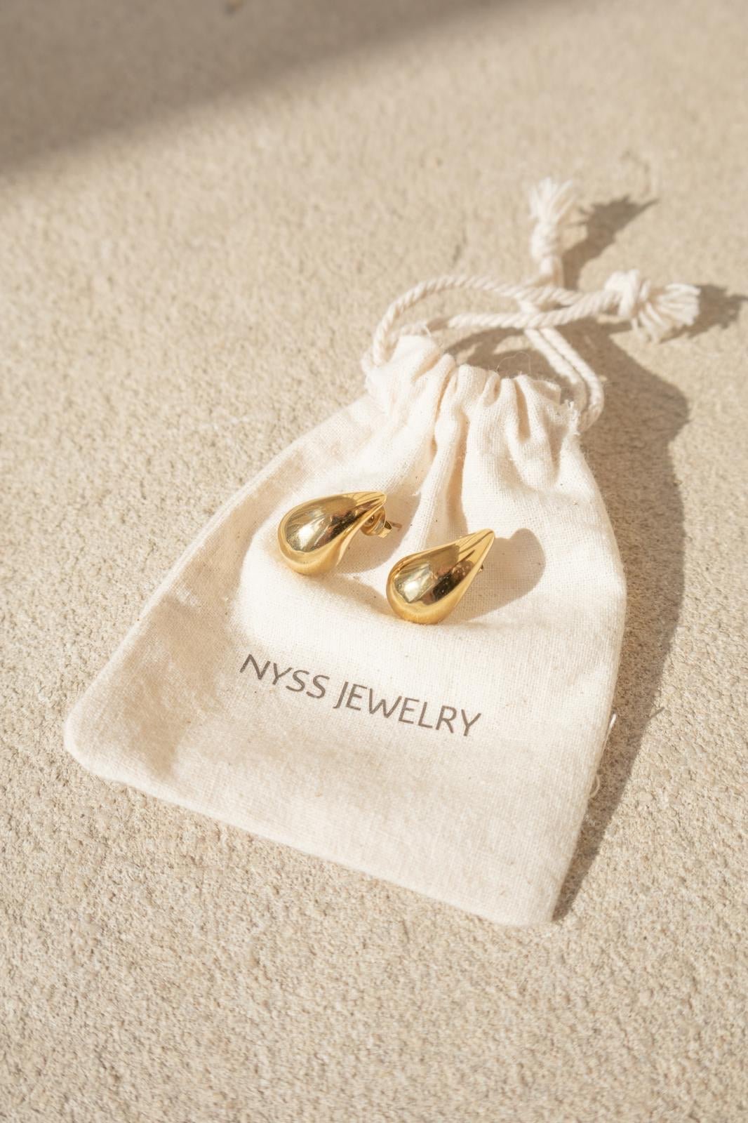 Boucles oreilles dorées présentées sur une pochettes Nyssary avec un fond sablé