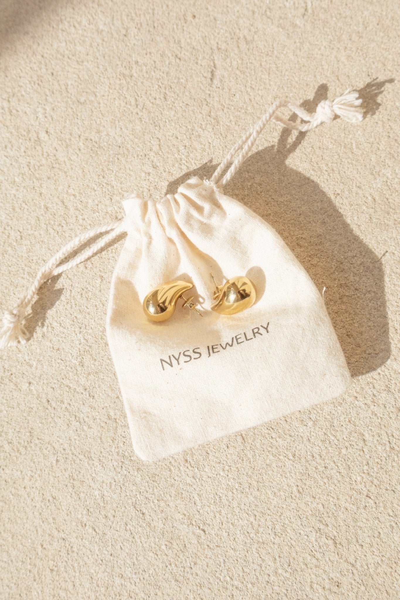 Boucles oreilles dorées présentées sur une pochettes Nyssary avec un fond sablé