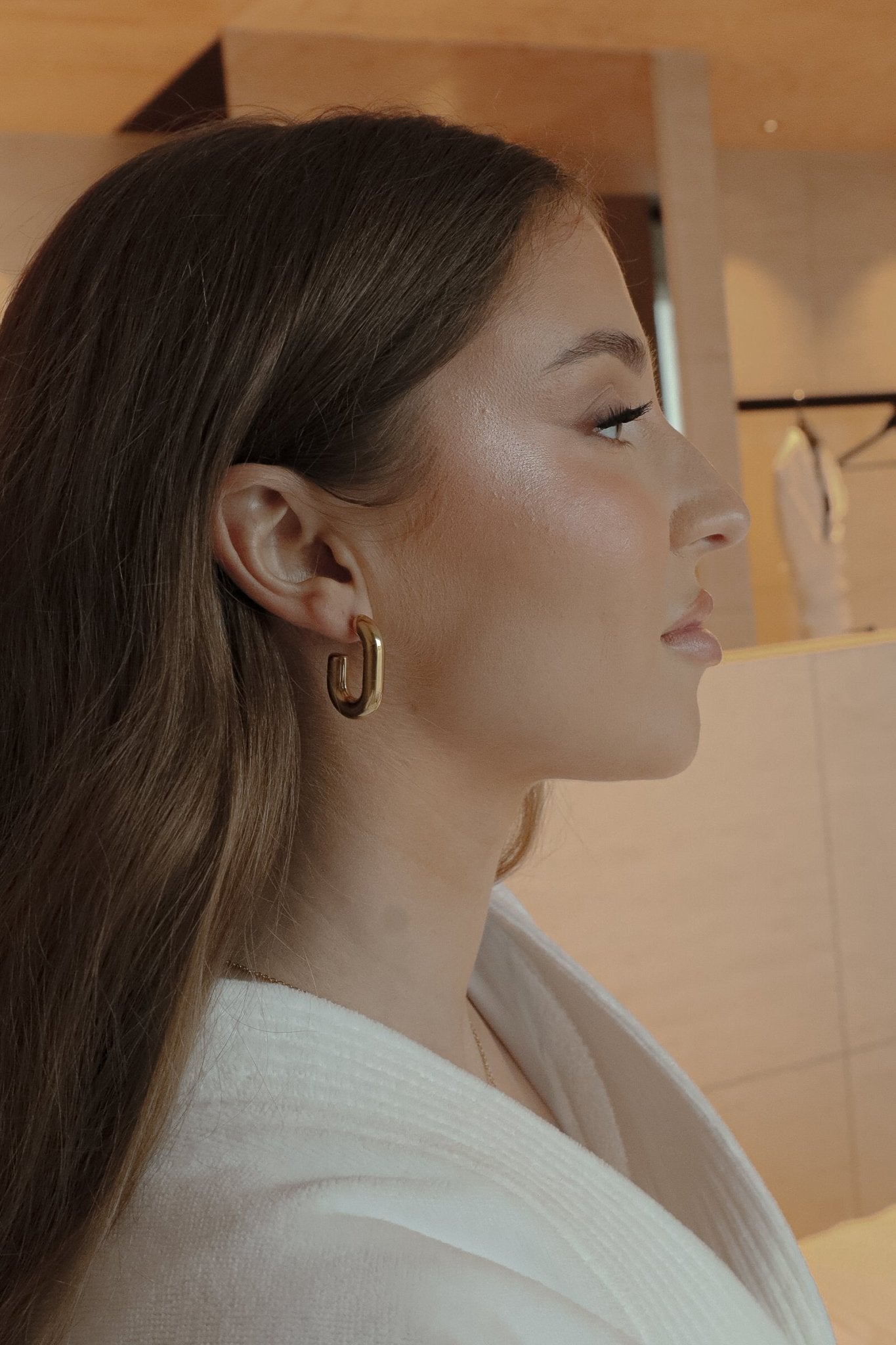 Visage zoomé d’une femme portant des boucles oreilles dorées, éclairées pour mettre en valeur leur brillance.