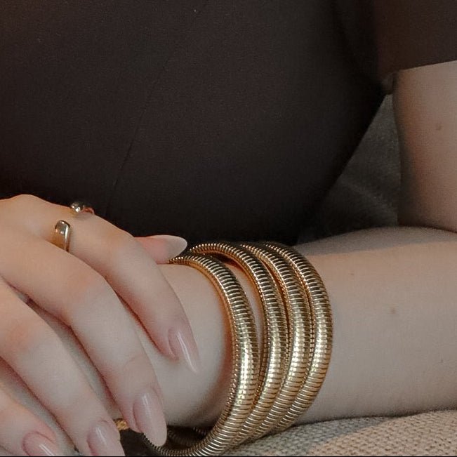 Femme portant une robe brune, mettant en valeur un bracelet doré en maille serpent autour de son poignet