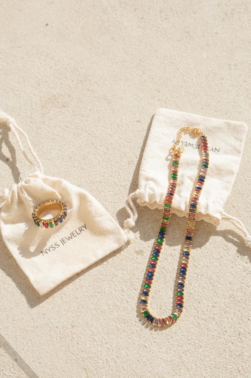 Collier acier inoxydable Arcadia avec strass multicolores, présenté sur des pochettes Nyssary avec un fond sablé