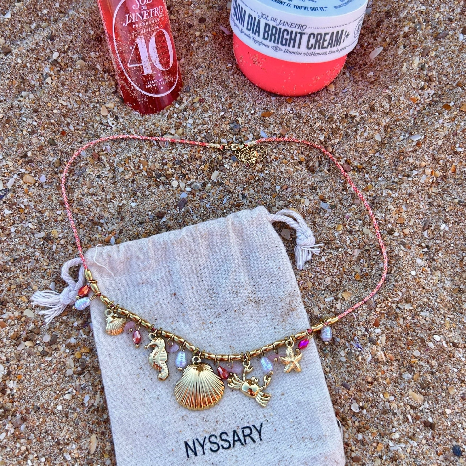 Collier doré Océane avec charms marins, présenté sur des pochettes Nyssary avec un fond sablé